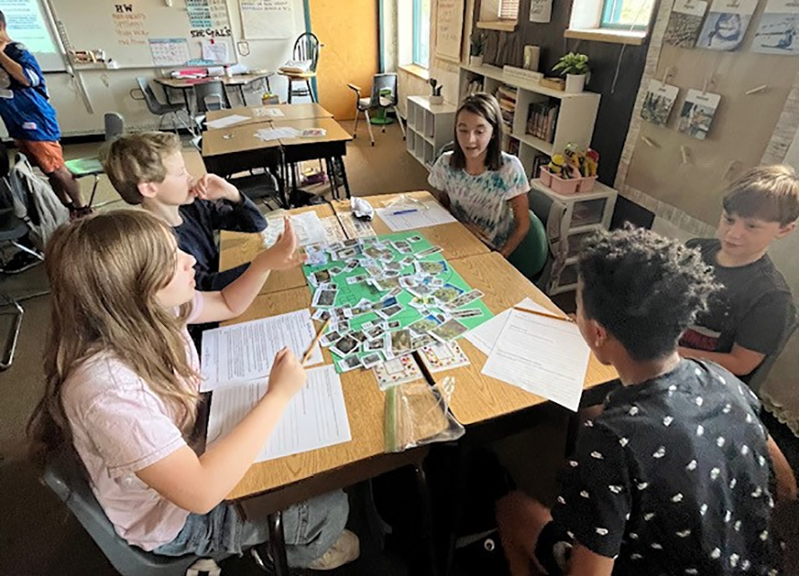 Four students sit at a table with worksheets