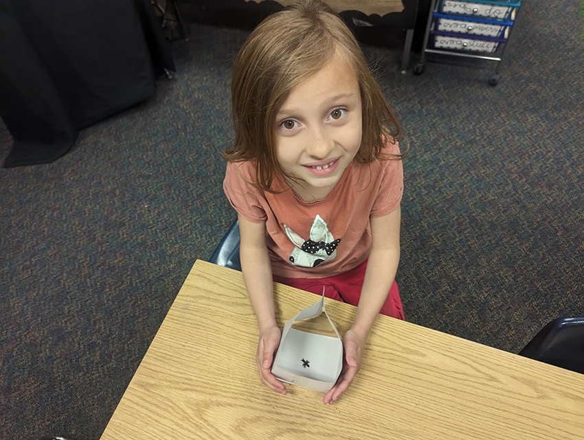 Young scientist looking at camera and holding a box containing a small invertebrate