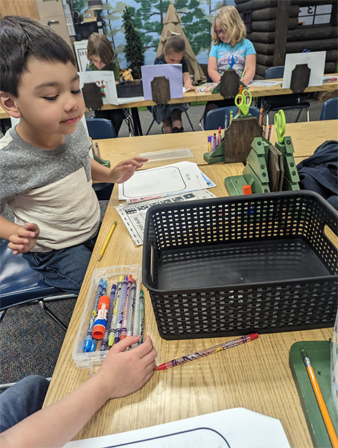 Young scientist with worksheets and crayons in front of him on a table